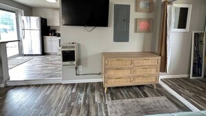 A modern kitchen with a built-in oven, a refrigerator, and a flat-screen TV mounted on the wall.