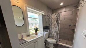 A bathroom with a shower, toilet, sink, and mirror.