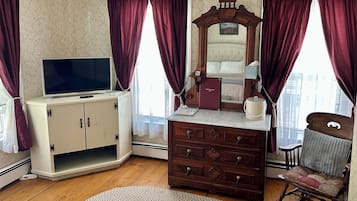 A room with a television, a dresser, a mirror, a rocking chair, and a window with curtains.