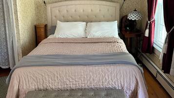 A bedroom with a bed, a nightstand, a wall clock, and a window with curtains.
