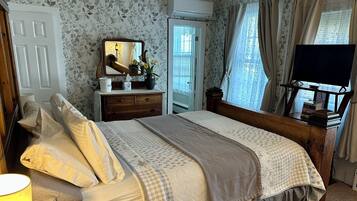A bedroom with a bed, dresser, mirror, and a television on a wooden stand.