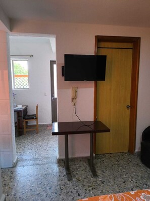 Ein Zimmer mit an der Wand montiertem Fernseher, einer Holztür, einem gefliesten Boden und einem Fenster mit Aussicht.