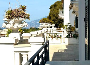 Ein weißes Gebäude mit Balkon, Geländer und Blick auf das Meer und die Berge.