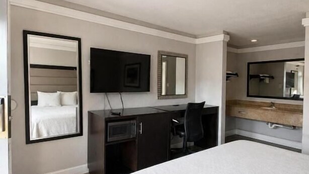 A modern hotel room with a large bed, a desk, a flat-screen TV, a mirror, and a wardrobe. - All Season Suites Inn  (Dallas)