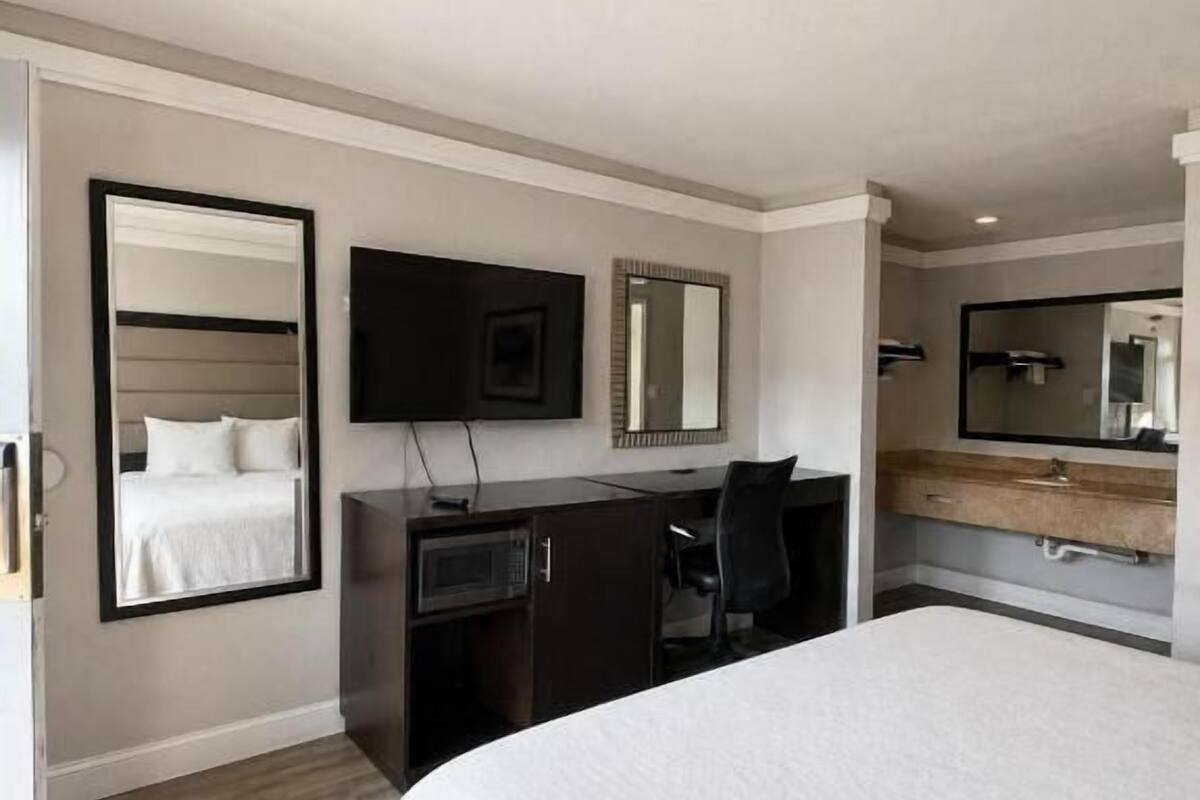 A modern hotel room with a large bed, a desk, a flat-screen TV, a mirror, and a wardrobe.