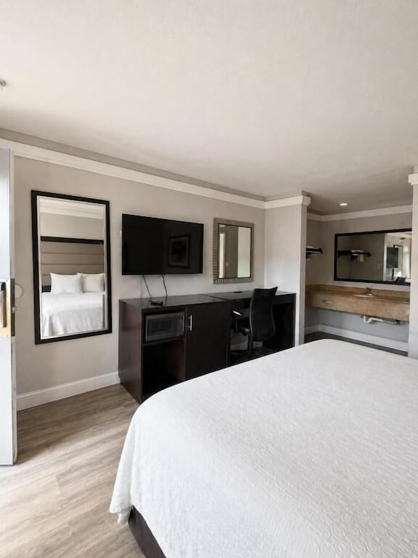 Moderni hotellihuone, jossa on suuri sänky, työpöytä, taulutelevisio, peili ja vaatekaappi.
