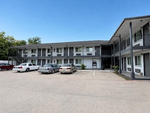 A multi-story motel with a parking lot, several cars parked, and a clear sky.