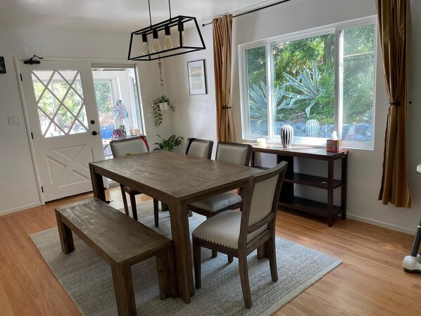 A dining room with a wooden table, chairs, a bench, a hanging light fixture, and a window with curtains.