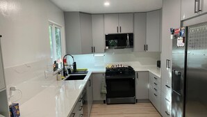 A modern kitchen with white cabinets, a stainless steel refrigerator, a microwave, and a stove. - Spacious 4-bedroom house with AC in tranquil Orinda (Orinda)