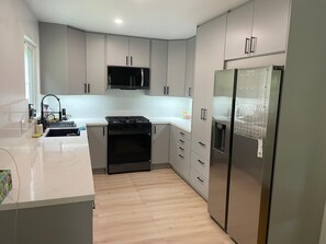 A modern kitchen with grey cabinets, a stainless steel refrigerator, a microwave, and a gas stove.
