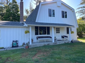 A white two-story house with a covered porch, a chimney, and a hose reel.