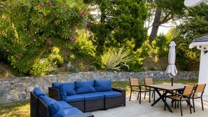 An outdoor patio area with a stone wall, a wicker sofa with blue cushions, a wooden table with chairs, and a white umbrella. - Spacious 4-bedroom house with AC in tranquil Orinda (Orinda)