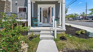 Une maison d’habitation avec un porche à l’avant, des marches menant à l’entrée et un espace extérieur aménagé pour s’asseoir.