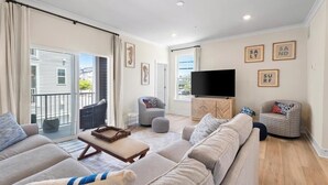 Un salon moderne avec un ensemble de canapés, un téléviseur à écran plat et un balcon agrémenté de rideaux.