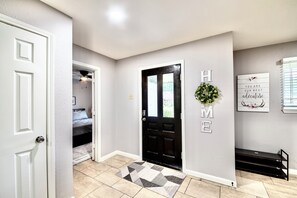 A hallway with a black door, a welcome sign, a bench, and a rug. - IAH to Downtown Hideaway -Pool table, Patio &Grill (Houston)
