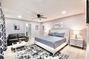 A bedroom with a bed, a nightstand, a coffee table, a sofa, a ceiling fan, and framed pictures on the wall. - IAH to Downtown Hideaway -Pool table, Patio &Grill (Houston)