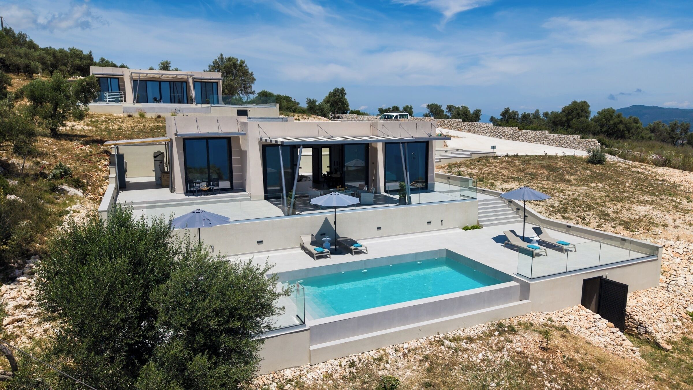 A modern villa with a swimming pool, outdoor seating, and a view of the surrounding landscape.