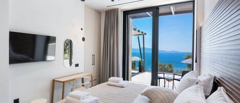 Una habitación de hotel moderna con cama, televisión, escritorio y balcón con vista al mar.