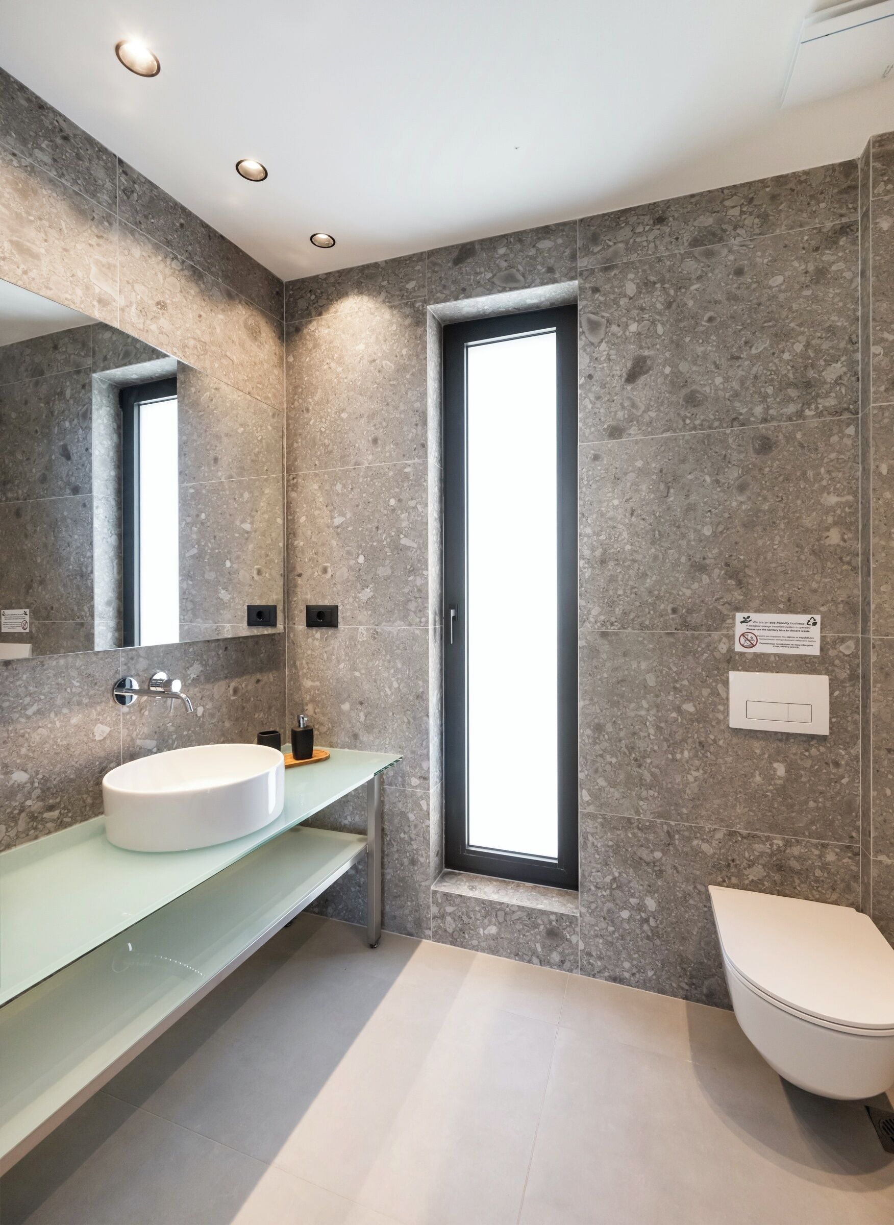 Un baño moderno con un espejo grande, un lavabo blanco, un inodoro y una ventana.