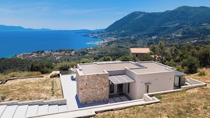 A modern building with a stone facade, flat roof, and a view of the sea and mountains.