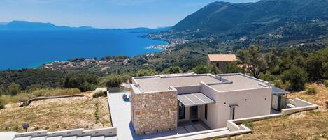A modern building with a stone facade, flat roof, and a view of the sea and mountains.