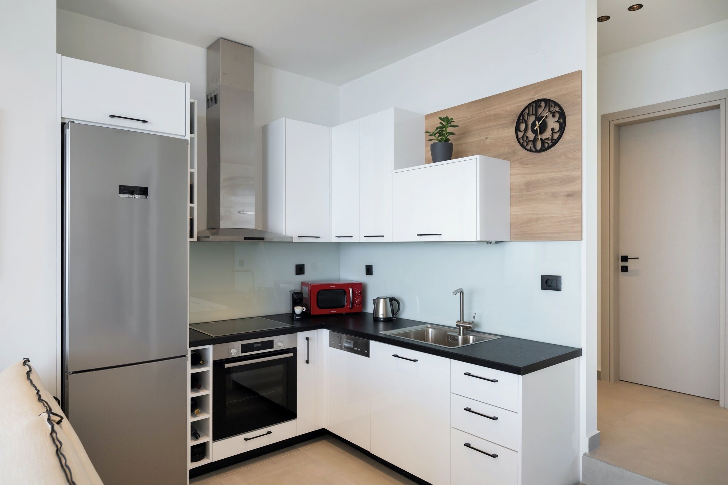 A modern kitchen with white cabinets, stainless steel appliances, a black countertop, and a wooden accent wall.