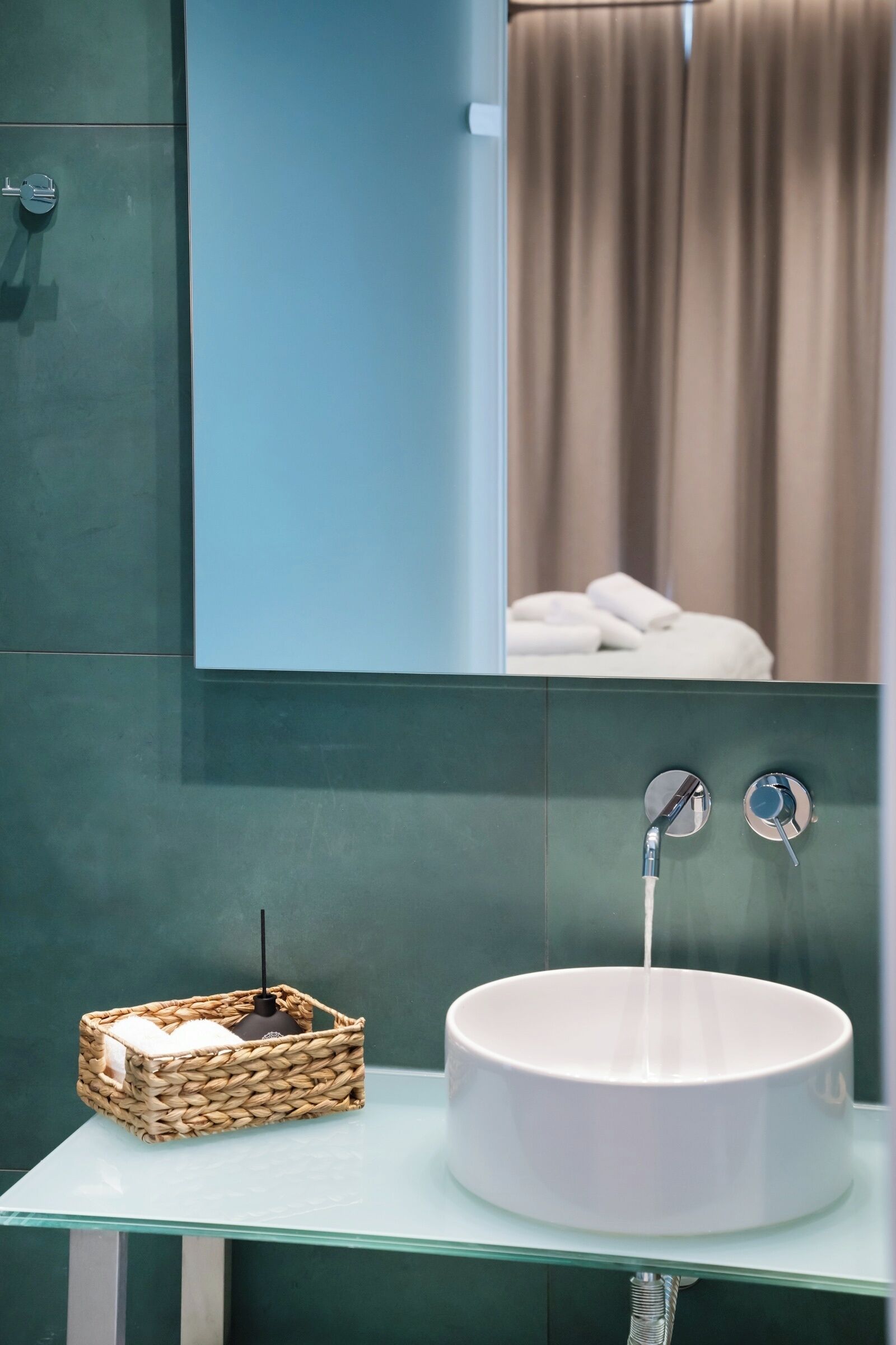 A bathroom with a white sink, a mirror, and a wicker basket on a glass countertop.