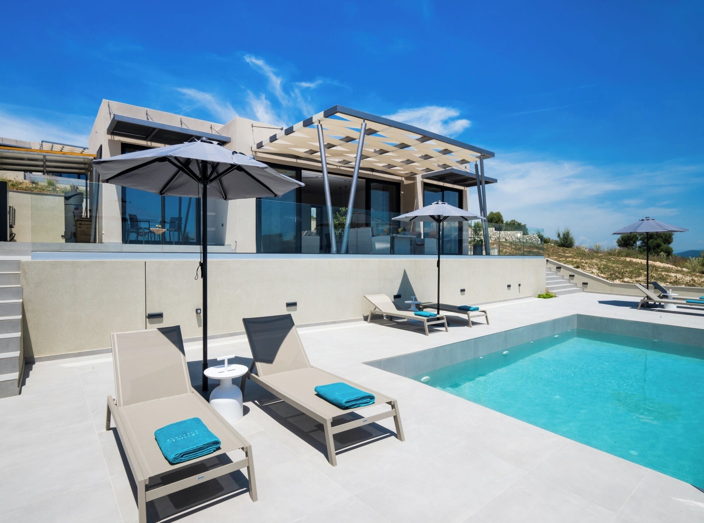 A modern pool area with lounge chairs and umbrellas, a clear blue sky, and a contemporary building in the background.