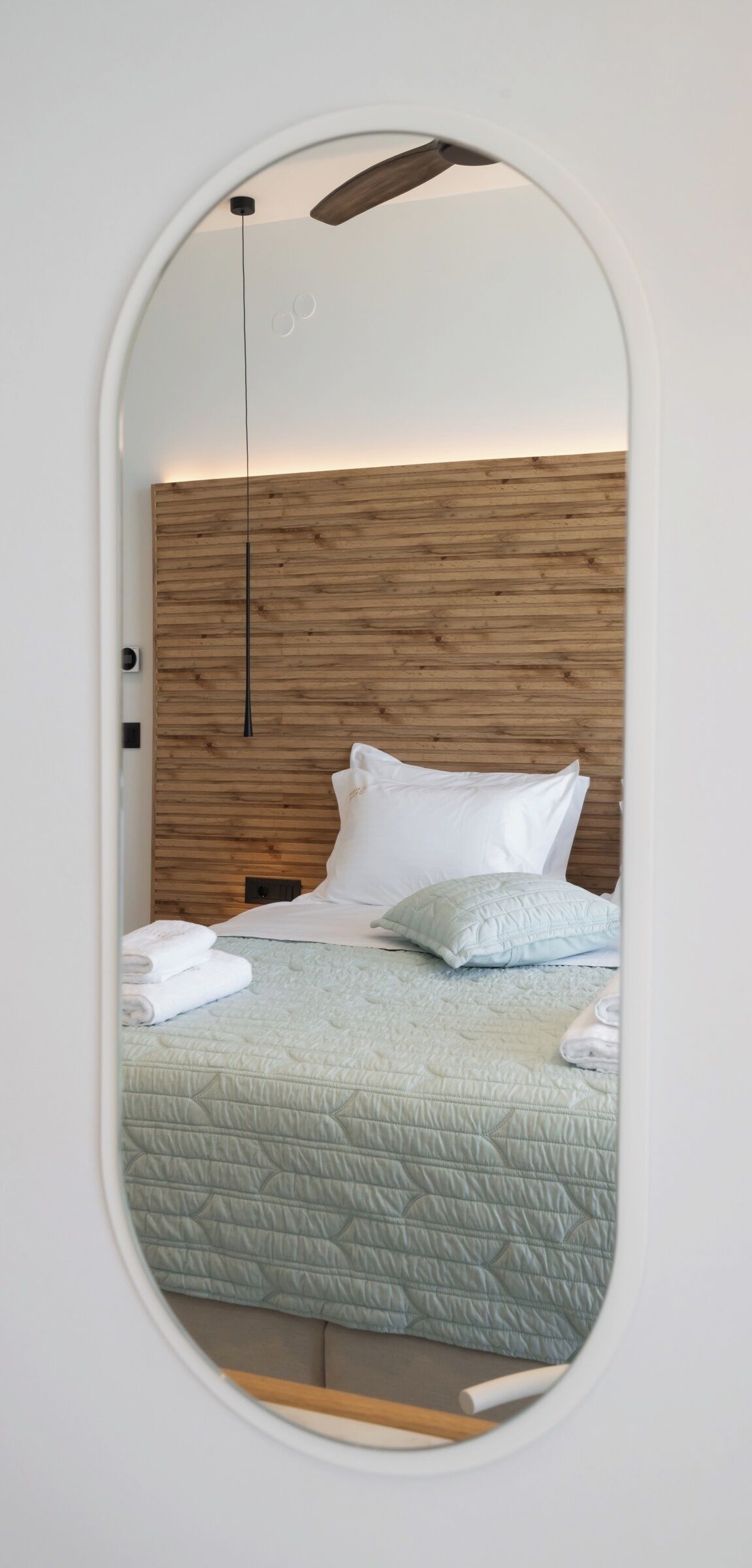 A room with a bed, a wooden headboard, a hanging light fixture, and a mirror on the wall.