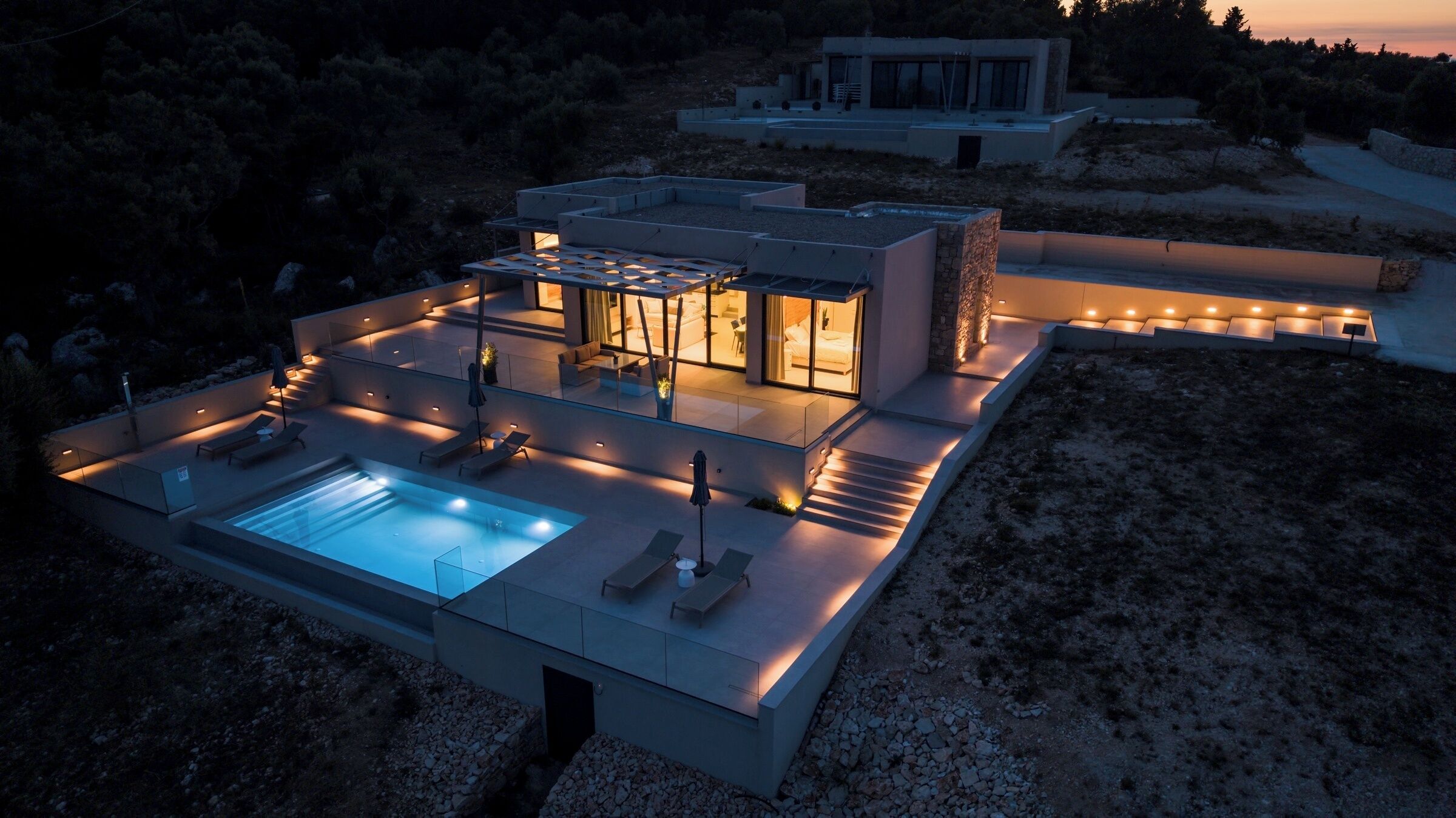 Una casa moderna con piscina, zona de estar exterior y un patio bien iluminado.