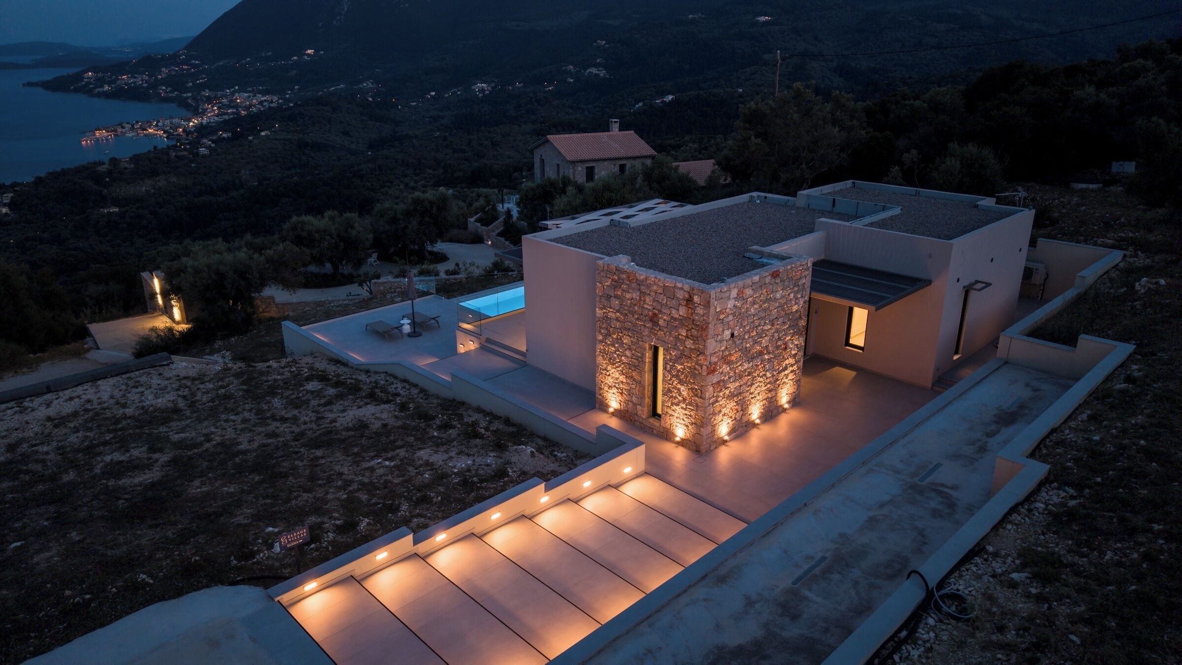 A modern house with a stone facade, a swimming pool, and a view of the sea.