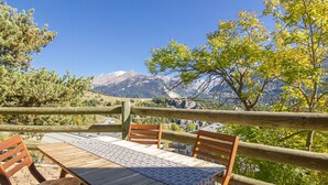 Taula de fusta amb caires, un llençol de taula amb motius i vista a la muntanya.