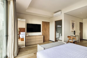 Habitación de hotel con cama, televisión, armario de madera, escritorio y baño visible a través de una puerta abierta.
