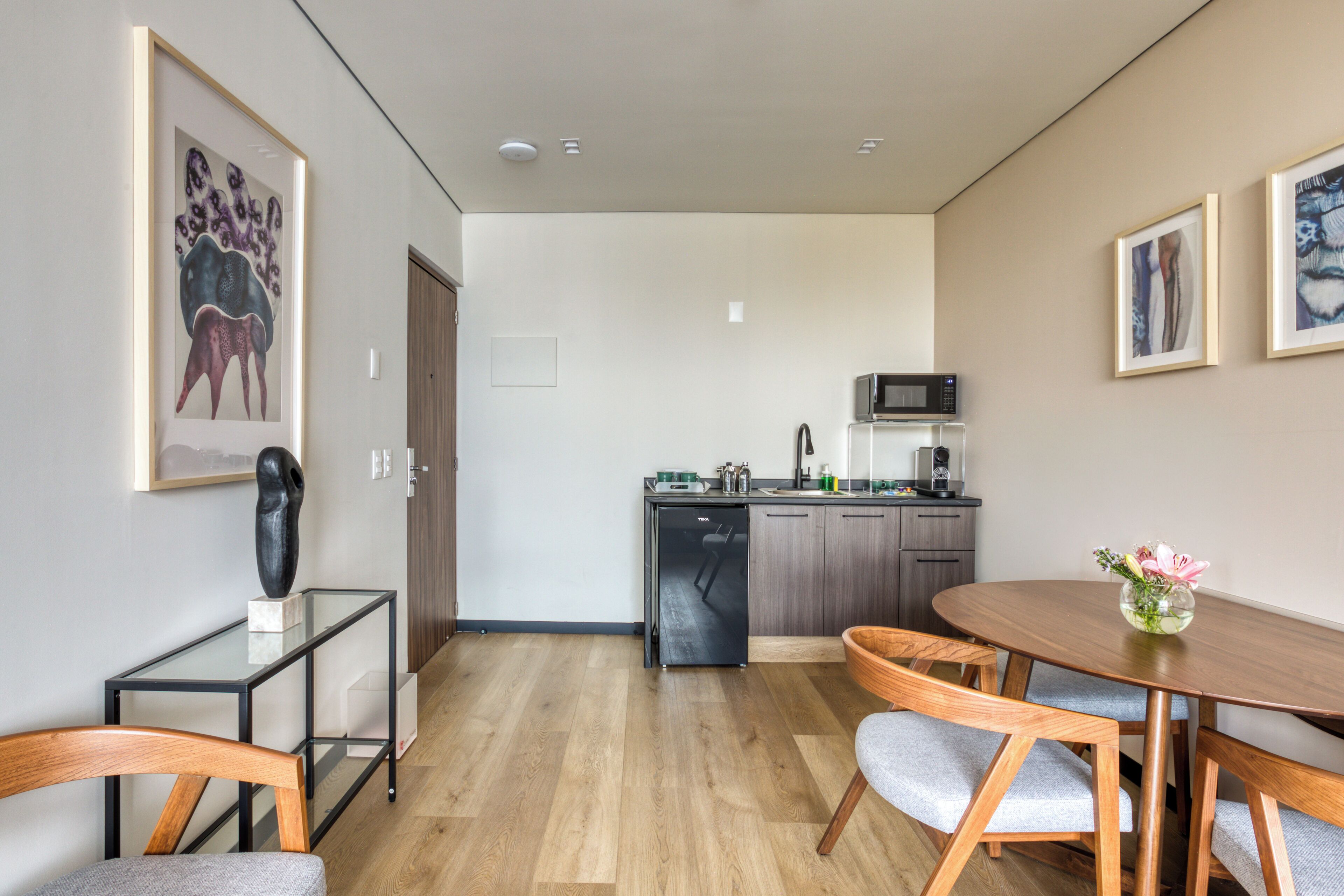 Une cuisine moderne équipée d’un four à micro-ondes, d’un évier et de placards. On y trouve une table à manger avec des chaises et un vase de fleurs.
