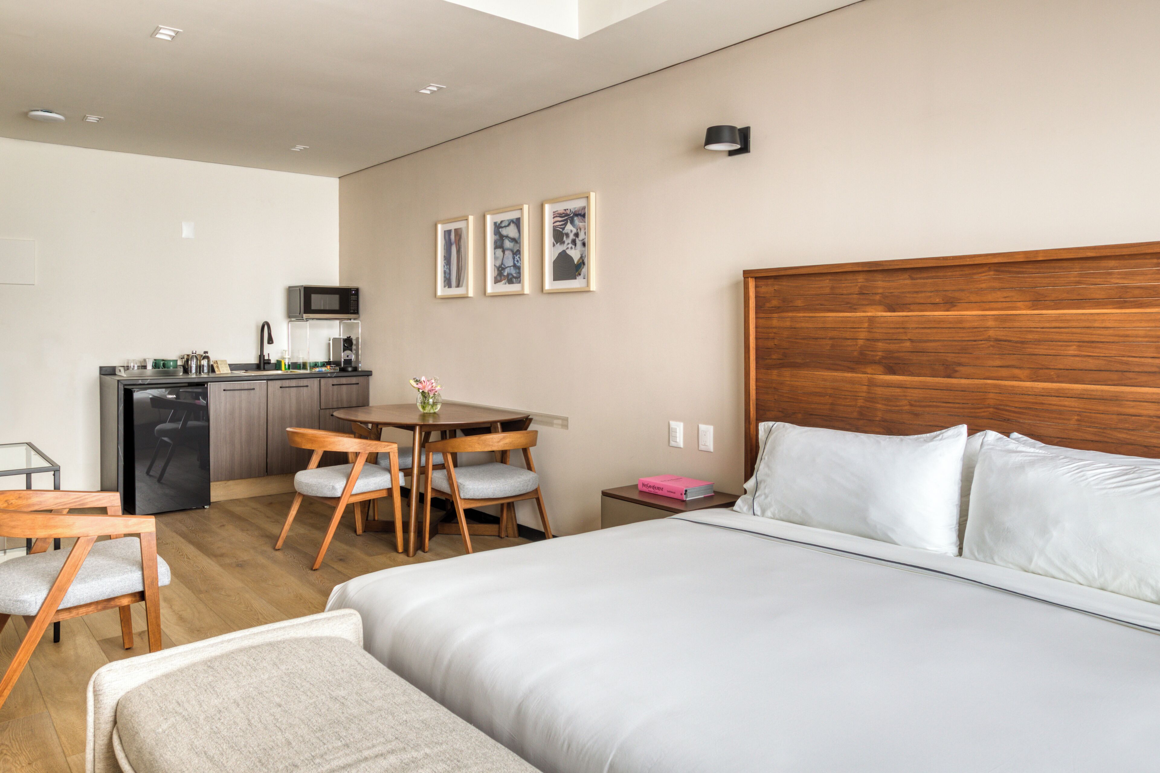 Habitación de hotel con cama, escritorio con silla, microondas, lavabo y una pequeña mesa con un florero.