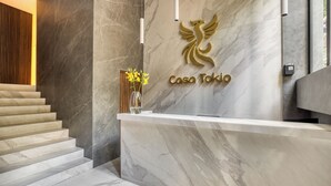 A reception desk with a marble wall, a logo, and a vase with yellow flowers. - Casa Tokio (Mexico City)