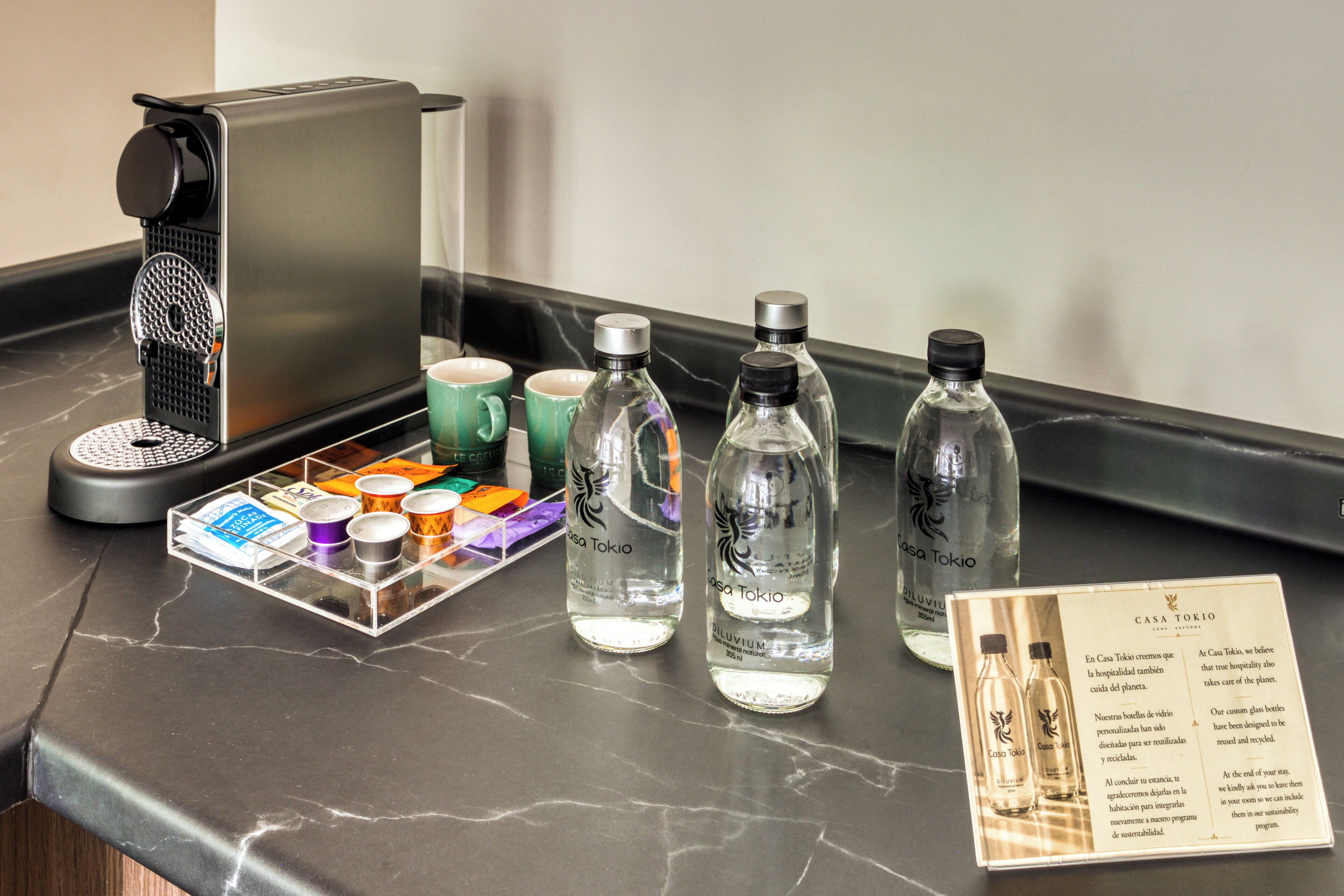 Un comptoir de cuisine avec une machine à café, trois bouteilles d’eau et un plateau contenant des tasses de différentes couleurs.