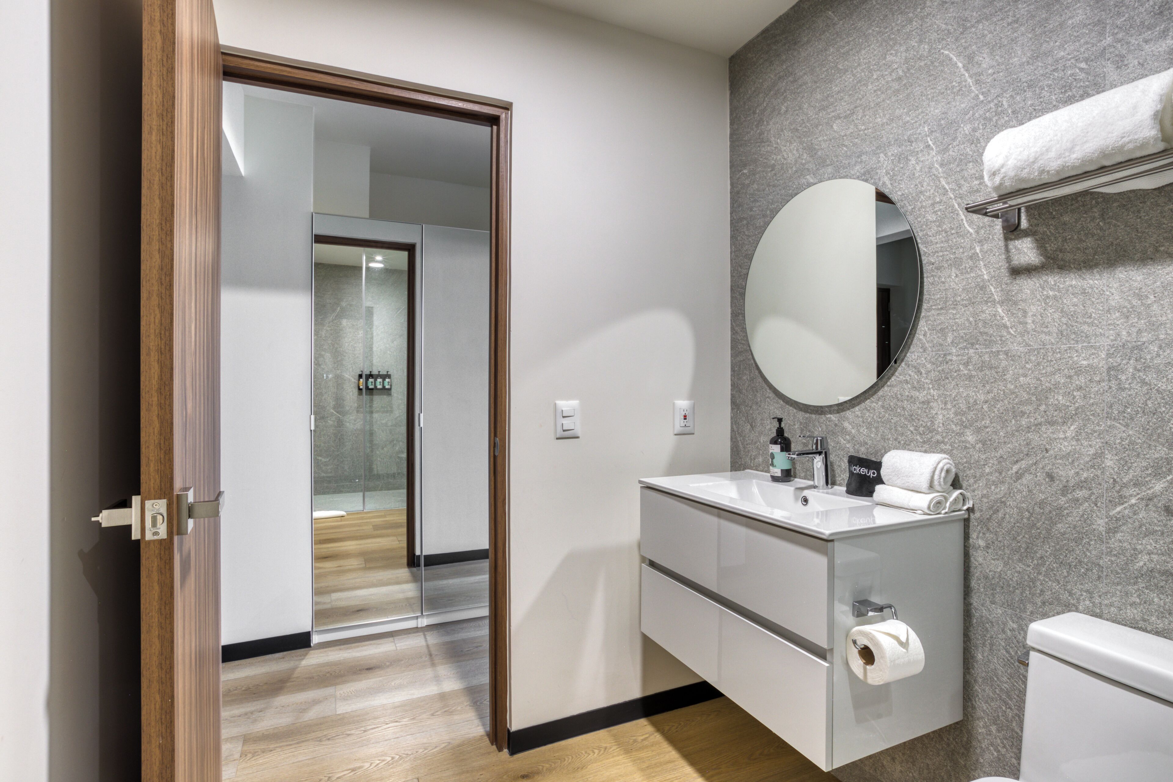 Une salle de bain moderne avec une porte de douche en verre, un miroir rond, un lavabo blanc et des toilettes.