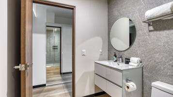 Une salle de bain moderne avec une porte de douche en verre, un miroir rond, un lavabo blanc et des toilettes.