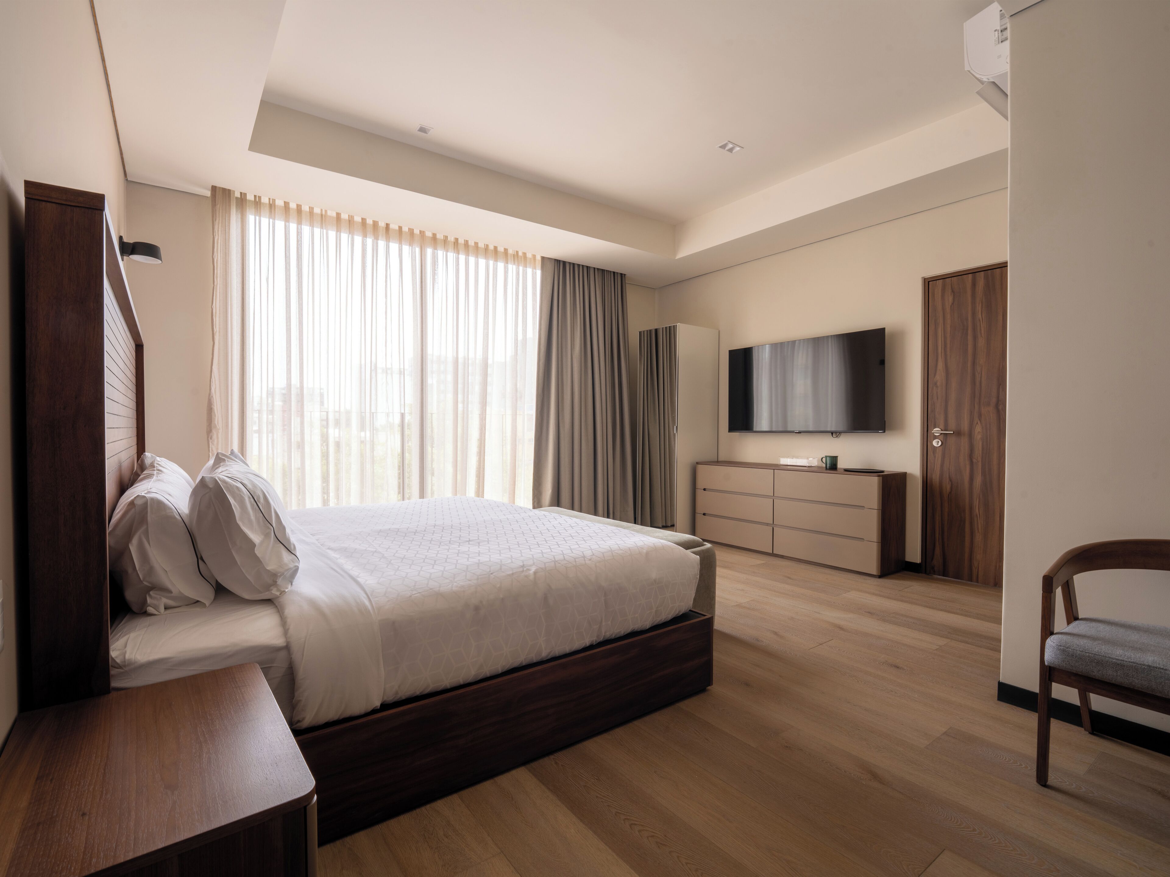 Ein modernes Hotelzimmer mit einem großen Bett, einem Fernseher, einem Kleiderschrank und einem Schreibtisch.