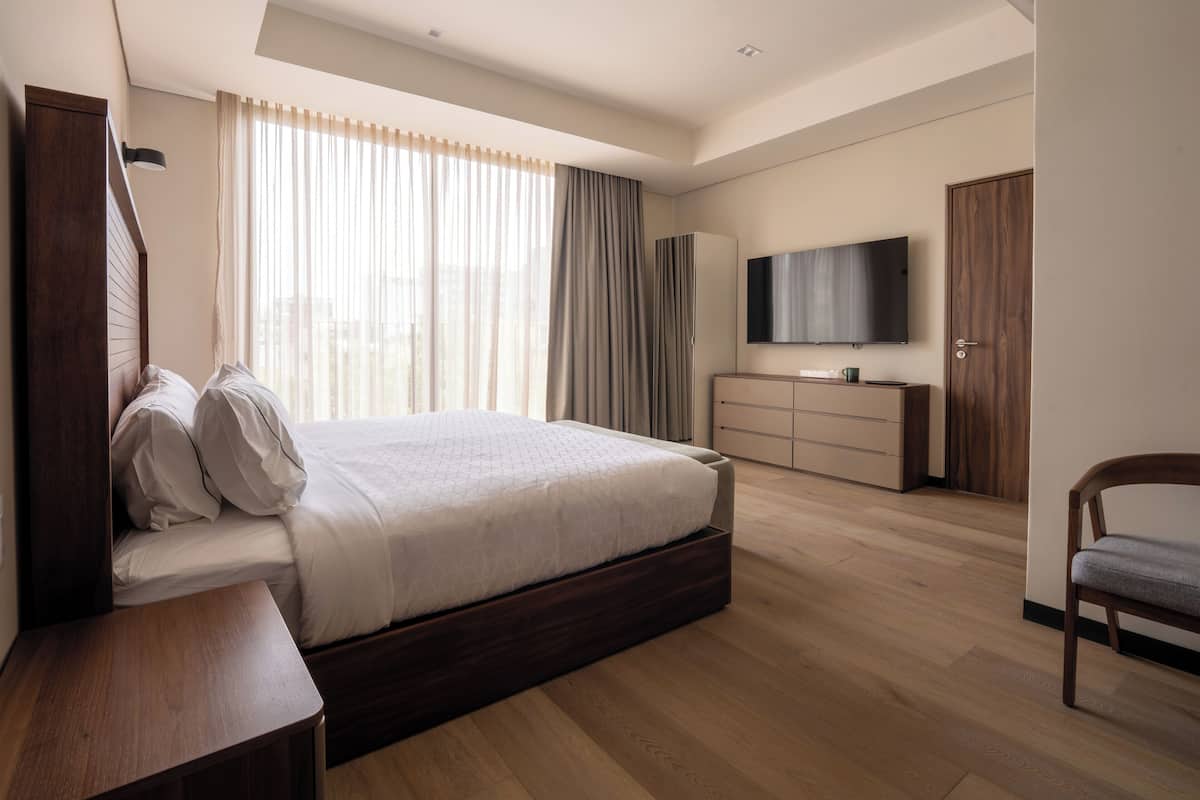 Ein modernes Hotelzimmer mit einem großen Bett, einem Fernseher, einem Kleiderschrank und einem Schreibtisch.