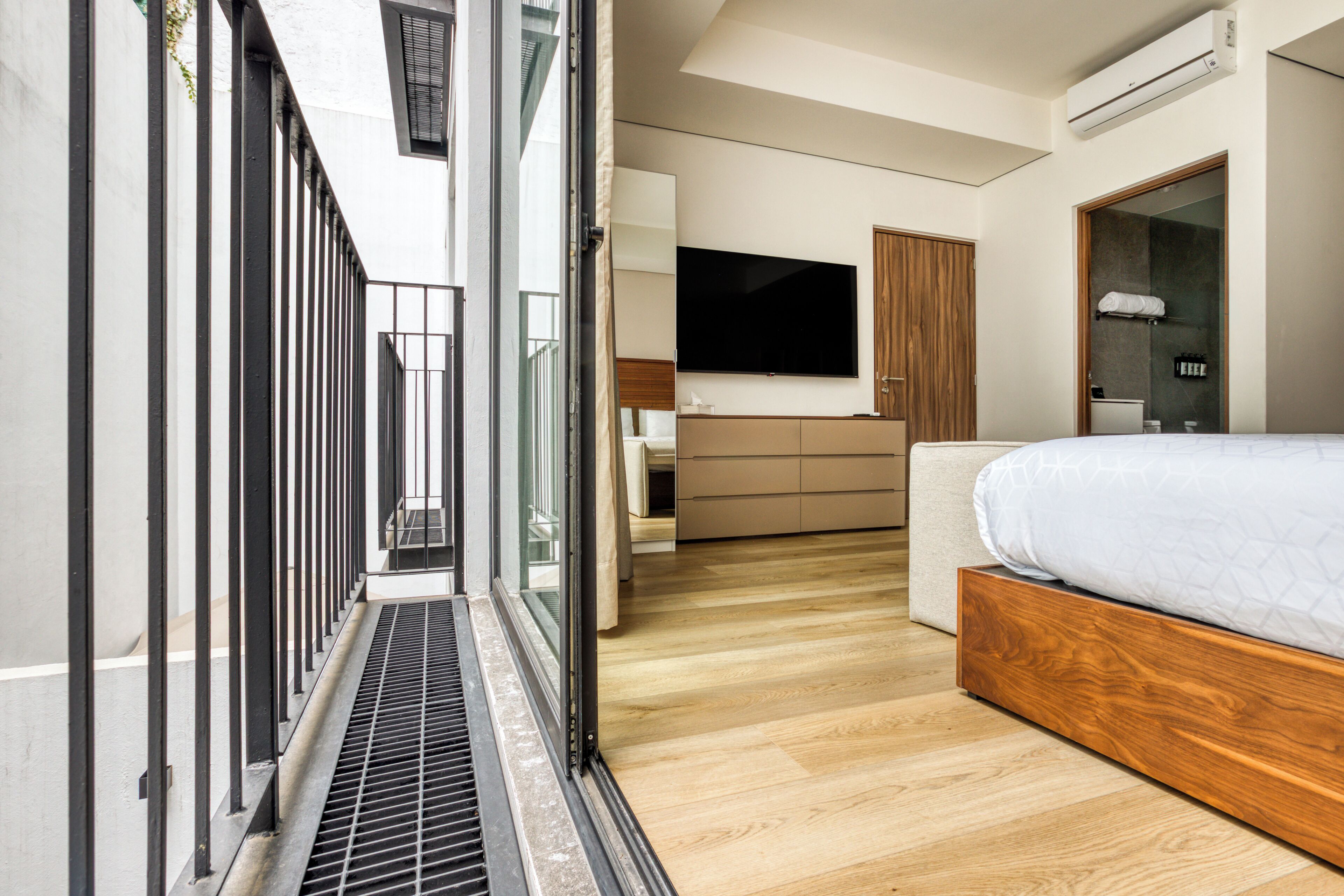 A modern hotel room with a large bed, a TV, a wooden wardrobe, and a balcony with a metal railing.