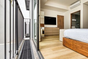 A modern hotel room with a large bed, a TV, a wooden wardrobe, and a balcony with a metal railing. - Casa Tokio (Mexico City)