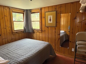 Una stanza con pannelli in legno, un letto, un quadro incorniciato, uno specchio e una finestra con tende.