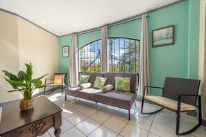 Ein Zimmer mit einer Couch, zwei Stühlen, einem Tisch mit einer Pflanze und einem Fenster mit Vorhängen.