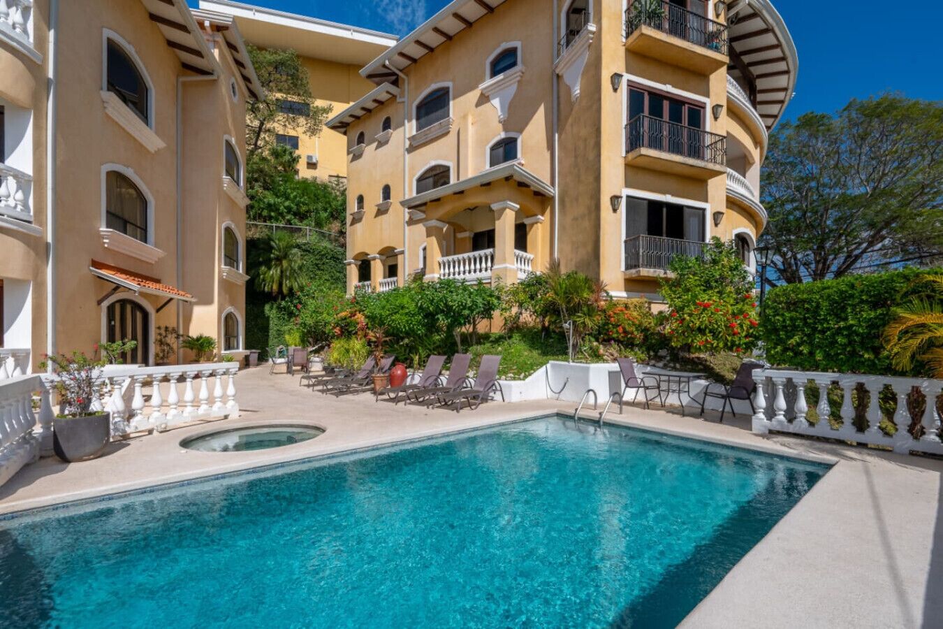 A hotel with a pool, lounge chairs, and a garden area.