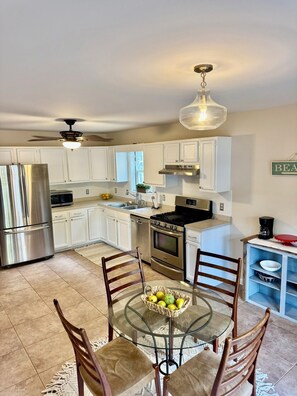 A modern kitchen with white cabinets, stainless steel appliances, a glass dining table, and a ceiling fan. - 3-bedroom house Near Masssy's boat ramp, Paradise Grill & Pot N Nets & Baywood (Millsboro)