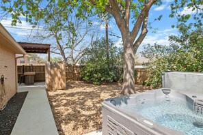 Un patio trasero con un jacuzzi, una valla de madera y un árbol.