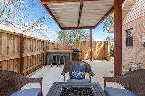 Eine Terrasse mit Rattanmöbeln, einem Grill und einem überdachten Bereich.