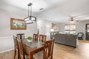 Un comedor con una mesa y sillas de madera, un ventilador de techo y un cuadro en la pared.
